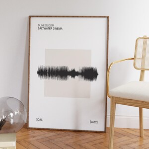 以下が含まれることがあります： 「DUNE BLOOM SALTWATER CINEMA」のテキストが、ベージュの背景に黒い音波のデザインの上に配置された、額装されたアートプリント。プリントには2023年と[4:07]のタイムスタンプが含まれています。フレームは濃い茶色です。