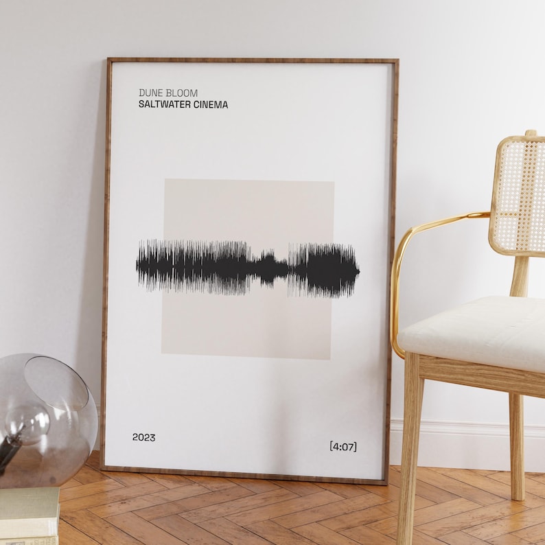 以下が含まれることがあります： 「DUNE BLOOM SALTWATER CINEMA」のテキストが、ベージュの背景に黒い音波のデザインの上に配置された、額装されたアートプリント。プリントには2023年と[4:07]のタイムスタンプが含まれています。フレームは濃い茶色です。