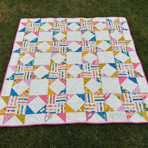 Puede incluir: Una colcha de retazos con fondo blanco y un patrón de estrellas rosas, amarillas y azules. La colcha está hecha de diferentes telas con varios patrones y texturas.