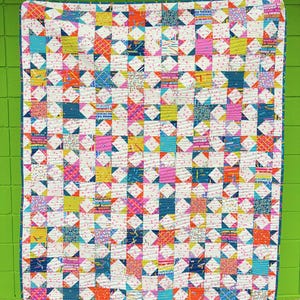 Puede incluir: Un edredón de patchwork colorido con un patrón de estrellas. El edredón presenta cuadrados de varios colores, incluyendo rosa, azul, amarillo y naranja, sobre un fondo blanco con pequeños lunares rosas. El edredón mide aproximadamente 152 cm por 178 cm.