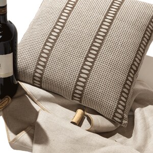 Puede incluir: Un coj&iacute;n de decoraci&oacute;n con estampado marr&oacute;n y blanco con una botella de vino y un corcho sobre un tejido de lino beige.