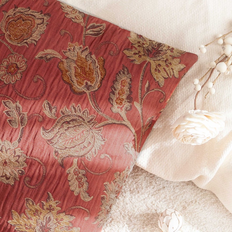 May include: A red throw pillow with a floral pattern in shades of brown and gold. The pillow is made of a textured fabric and has a subtle sheen.
