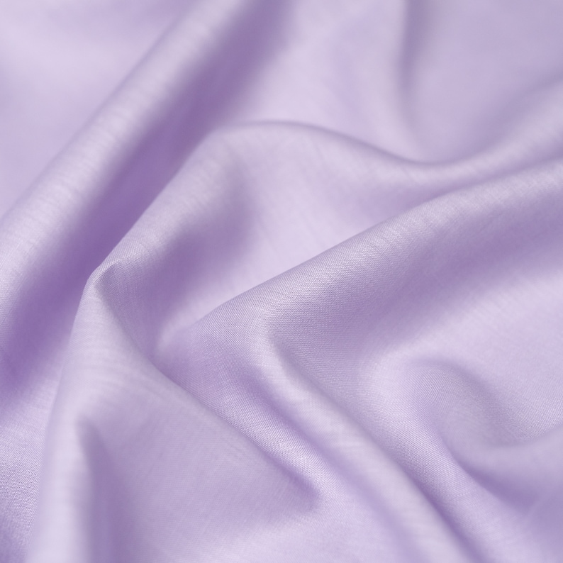 May include: A close-up of a smooth, soft, light purple fabric. The fabric is draped and folded, creating a luxurious and elegant look.