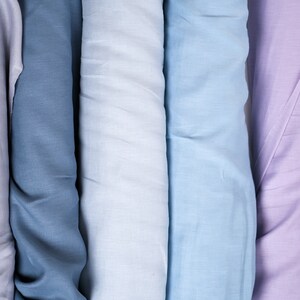 May include: Four rolls of fabric in different shades of blue and purple. The fabric is smooth and has a subtle texture.