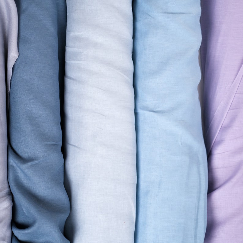 May include: Four rolls of fabric in different shades of blue and purple. The fabric is smooth and has a subtle texture.