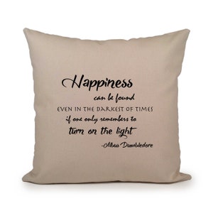 Puede incluir: Cojín beige con texto negro que dice "Happiness can be found even in the darkest of times if one only remembers to turn on the light -Albus Dumbledore"