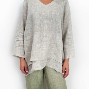 May include: A beige linen top with a V-neck and a layered, asymmetrical hem. The top has long sleeves and is made of a lightweight, breathable fabric.