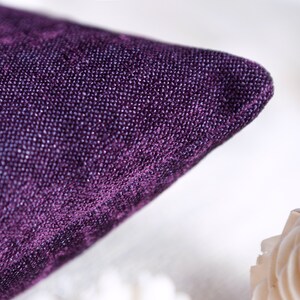 May include: Close-up of a deep purple velvet pillow with a textured surface.