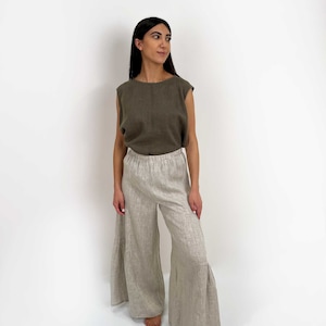 May include: A sleeveless olive green top with a round neckline paired with wide-leg beige trousers featuring an elastic waistband and a tiered, flared hemline. The outfit is constructed from a textured fabric with a visible weave throughout the garment.