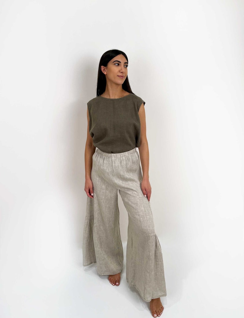 May include: A sleeveless olive green top with a round neckline paired with wide-leg beige trousers featuring an elastic waistband and a tiered, flared hemline. The outfit is constructed from a textured fabric with a visible weave throughout the garment.
