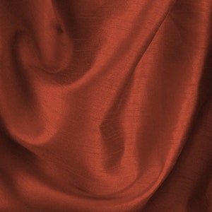 May include: A close-up of a rust-coloured fabric with a smooth, silky texture. The fabric is draped and folded, creating soft, flowing lines.