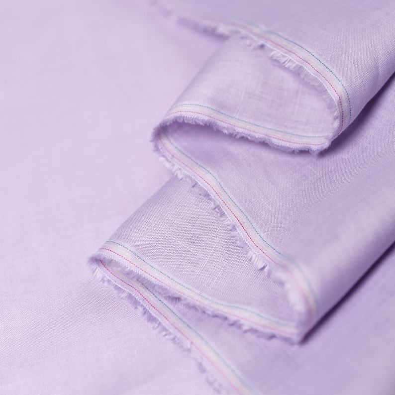 May include: A close-up of a light purple fabric with a white and red trim. The fabric is folded and the edges are frayed.