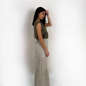May include: An olive green sleeveless top with wide shoulders paired with a floor-length, tiered skirt in a light beige, natural linen-like texture. The skirt features an elasticized waistband and a relaxed, flowing silhouette that reaches the ankles.