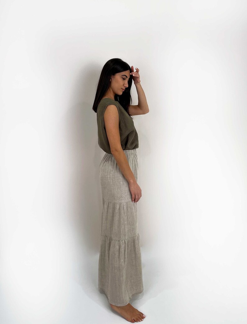 May include: An olive green sleeveless top with wide shoulders paired with a floor-length, tiered skirt in a light beige, natural linen-like texture. The skirt features an elasticized waistband and a relaxed, flowing silhouette that reaches the ankles.