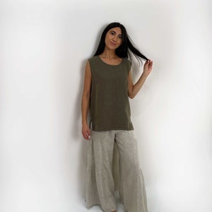 May include: A sleeveless olive green top with a round neckline and side slits paired with wide-leg beige pants featuring a tiered design. The garments are made of a textured fabric and have a loose, relaxed fit that falls to the ankles.