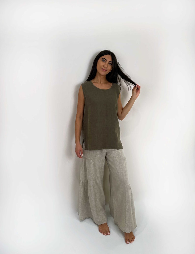 May include: A sleeveless olive green top with a round neckline and side slits paired with wide-leg beige pants featuring a tiered design. The garments are made of a textured fabric and have a loose, relaxed fit that falls to the ankles.