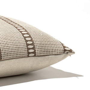 Puede incluir: Una almohada beige con un patr&oacute;n geom&eacute;trico marr&oacute;n que presenta peque&ntilde;os puntos y formas ovaladas m&aacute;s grandes. La almohada tiene una cremallera.