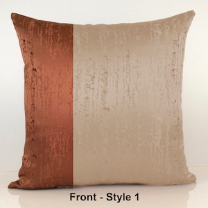 May include: A decorative throw pillow with a two-tone design. One side is a rich copper color, while the other side is a light beige. The pillow has a textured fabric with a subtle sheen.