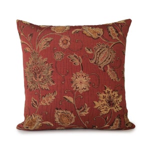 May include: A red throw pillow with a floral pattern in shades of brown and gold. The pillow has a square shape and a soft, textured fabric.