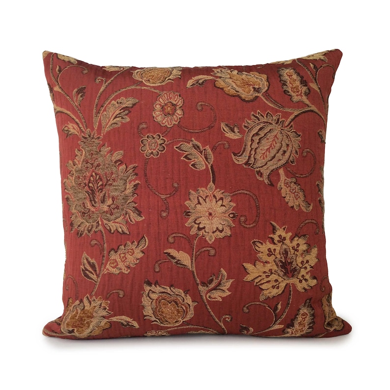 May include: A red throw pillow with a floral pattern in shades of brown and gold. The pillow has a square shape and a soft, textured fabric.