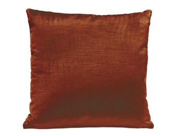 May include: A square, rust-colored decorative pillow. The pillow has a soft, velvety texture and a subtle sheen. The solid color and simple design make it a versatile accent piece for any room. The pillow is approximately 18 inches square.