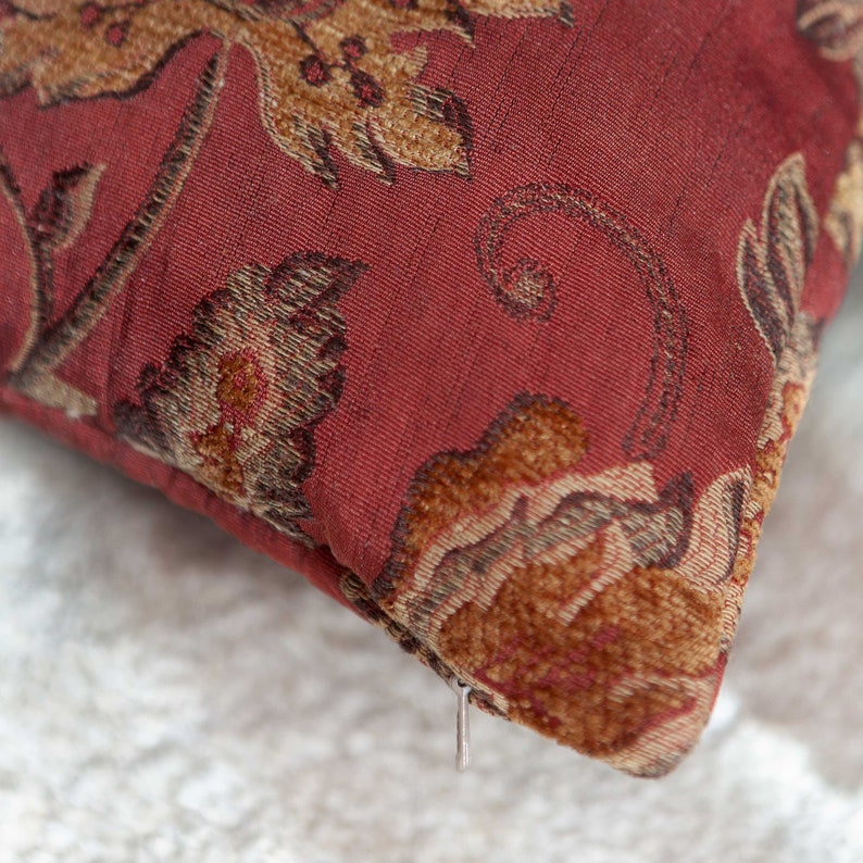 May include: A red throw pillow with a floral pattern in shades of brown and gold. The pillow has a zipper closure.