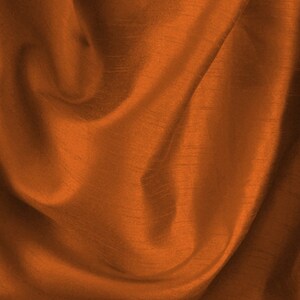 May include: A close-up of a rust-coloured fabric with a smooth, silky texture. The fabric is draped and folded, creating soft, flowing lines.