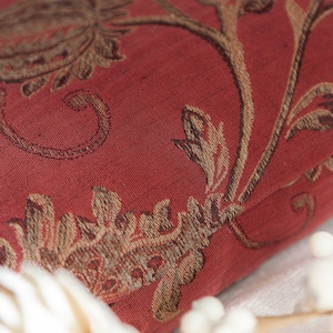 May include: Close-up of a red fabric with a gold floral pattern. The fabric has a textured, woven look.