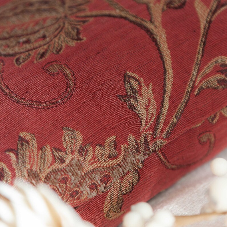 May include: Close-up of a red fabric with a gold floral pattern. The fabric has a textured, woven look.