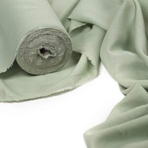 May include: A roll of sage green fabric with a slightly textured surface. The fabric is folded and draped on a white background.