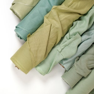 May include: A stack of five different colored fabric swatches in shades of green. The fabric is soft and flowing, with a subtle sheen.