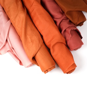May include: Four rolls of fabric in shades of orange, pink, and red. The fabric is a linen blend and has a soft, textured feel.