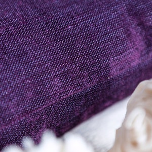 May include: Close-up of a deep purple fabric with a textured, woven pattern. The fabric has a subtle sheen and a soft, luxurious feel.