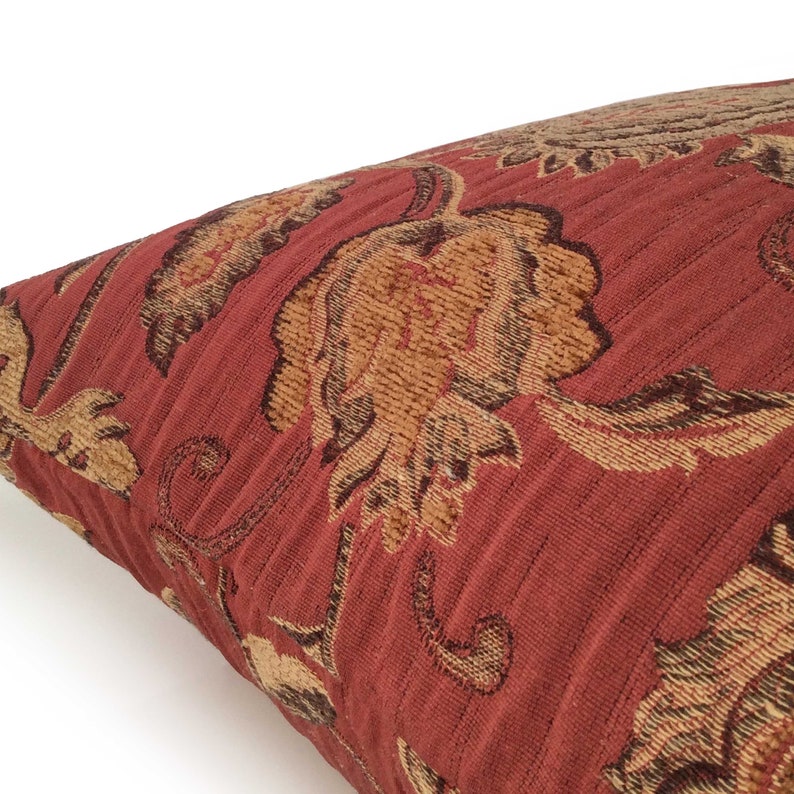 May include: A red pillow with a floral pattern in shades of brown and gold. The pillow is made of a textured fabric and has a subtle sheen.