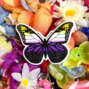 May include: A sticker of a purple, yellow, and white butterfly with black wings. The butterfly is on a background of colorful artificial flowers.