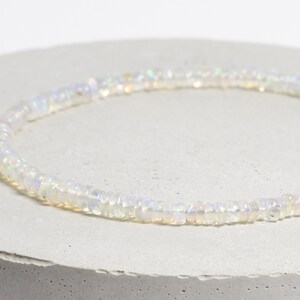 May include: A white opal beaded necklace with iridescent shimmer. The necklace is made of small, round beads and is strung on a thin, silver chain.