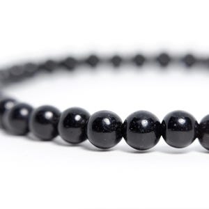May include: A bracelet composed of a single strand of smooth, polished, spherical black beads. The beads are uniform in size and shape, arranged in a continuous circular pattern, reflecting light on their glossy, dark surfaces.
