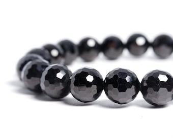 May include: A close-up of a black beaded bracelet. The beads are faceted, giving them a multi-dimensional appearance. The bracelet is set against a white background, highlighting the dark color and texture of the beads.