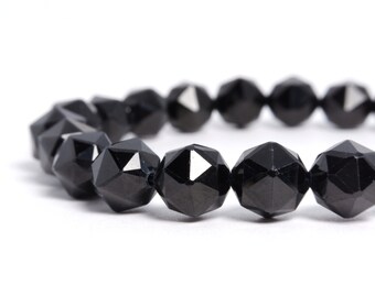 May include: A close-up of a black beaded bracelet. The beads are faceted, with multiple geometric sides that catch the light. The bracelet is on a white background, highlighting the dark color and shape of the beads.