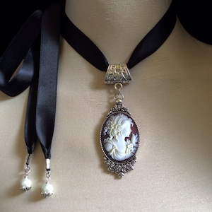 Beautiful, detailed, light ivory and dark wine cameo set in an oval, antique silver pendant with tiny baroque roses and attached to a high quality double sided satin ribbon...round, light ivory pearls are attached to each end of the 25" ties....