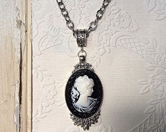 May include: A silver chain necklace with a black and white cameo pendant featuring a woman's profile.