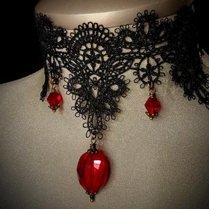 Op de afbeelding: Een zwarte kanten choker ketting met drie hangende rode edelsteen hangers.