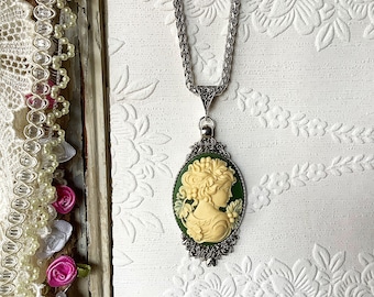 May include: A silver chain necklace with a green and white cameo pendant featuring a woman's profile. The cameo is set in a silver frame with ornate details.
