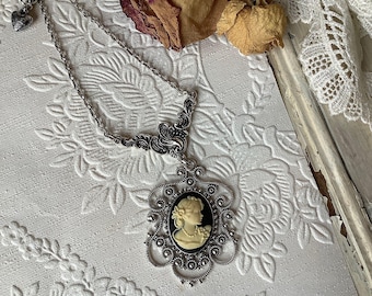 Op de afbeelding: Een zilveren ketting met een cameo-hanger met het profiel van een vrouw in zwart-wit. De cameo is omgeven door een delicaat zilveren filigraanontwerp.