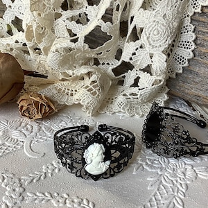 May include: Two black metal bracelets with intricate filigree designs. One bracelet features a white cameo with a woman's profile.