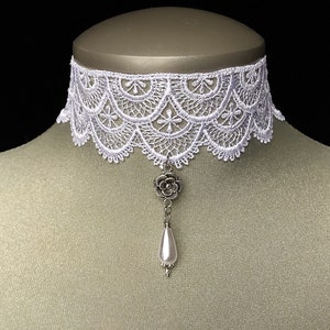 May include: White lace choker necklace with a silver flower pendant and a pearl drop. The choker is delicate and feminine, perfect for adding a touch of elegance to any outfit.