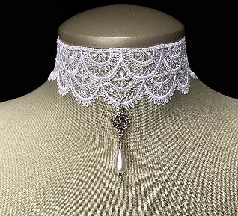 May include: White lace choker necklace with a silver flower pendant and a pearl drop. The choker is delicate and feminine, perfect for adding a touch of elegance to any outfit.