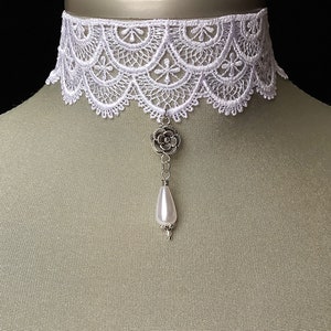 May include: White lace choker necklace with a silver flower pendant and a pearl drop.