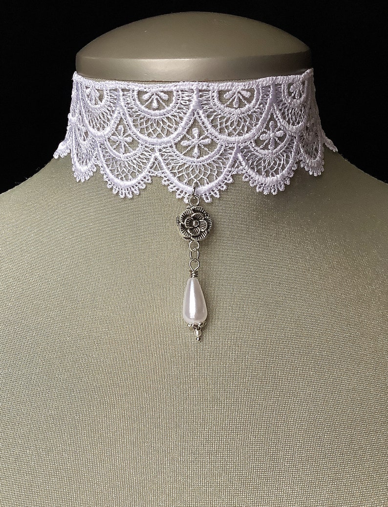 May include: White lace choker necklace with a silver flower pendant and a pearl drop.
