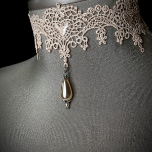 May include: A delicate ivory lace choker with a single pearl pendant. The choker is made of a fine, intricate lace pattern and is accented with a small, elegant pearl.